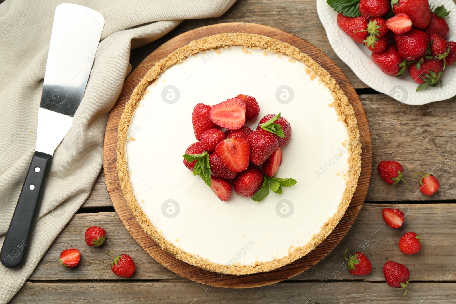 Tasty cheesecake with strawberries, mint and server on wooden table, flat lay Photo of Tasty cheesecake with strawberries, mint and server on wooden table, flat lay
