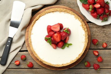 Photo of Tasty cheesecake with strawberries, mint and server on wooden table, flat lay