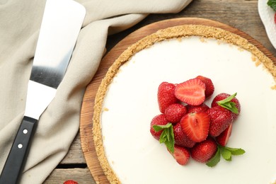 Photo of Tasty cheesecake with strawberries, mint and server on wooden table, flat lay
