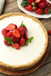 Photo of Tasty cheesecake with strawberries and mint on wooden table