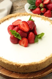 Photo of Tasty cheesecake with strawberries and mint on wooden table, closeup