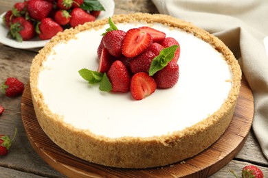Photo of Tasty cheesecake with strawberries and mint on wooden table, closeup