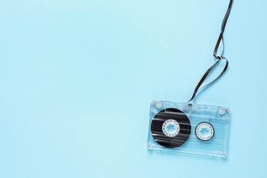 Photo of One audio cassette with magnetic tape on light blue background, top view. Space for text