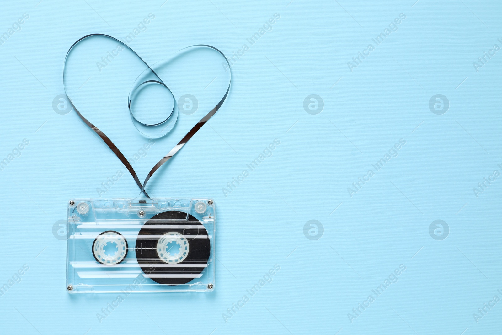One audio cassette with heart shaped magnetic tape on light blue background, top view. Space for text Photo of One audio cassette with heart shaped magnetic tape on light blue background, top view. Space for text