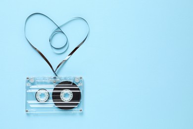 Photo of One audio cassette with heart shaped magnetic tape on light blue background, top view. Space for text