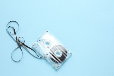Photo of One audio cassette with magnetic tape on light blue background, top view. Space for text