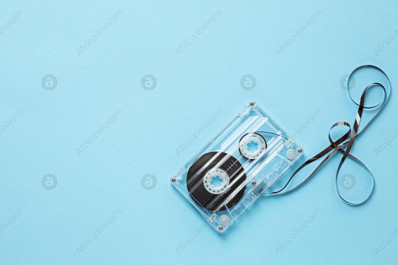 Photo of One audio cassette with magnetic tape on light blue background, top view. Space for text