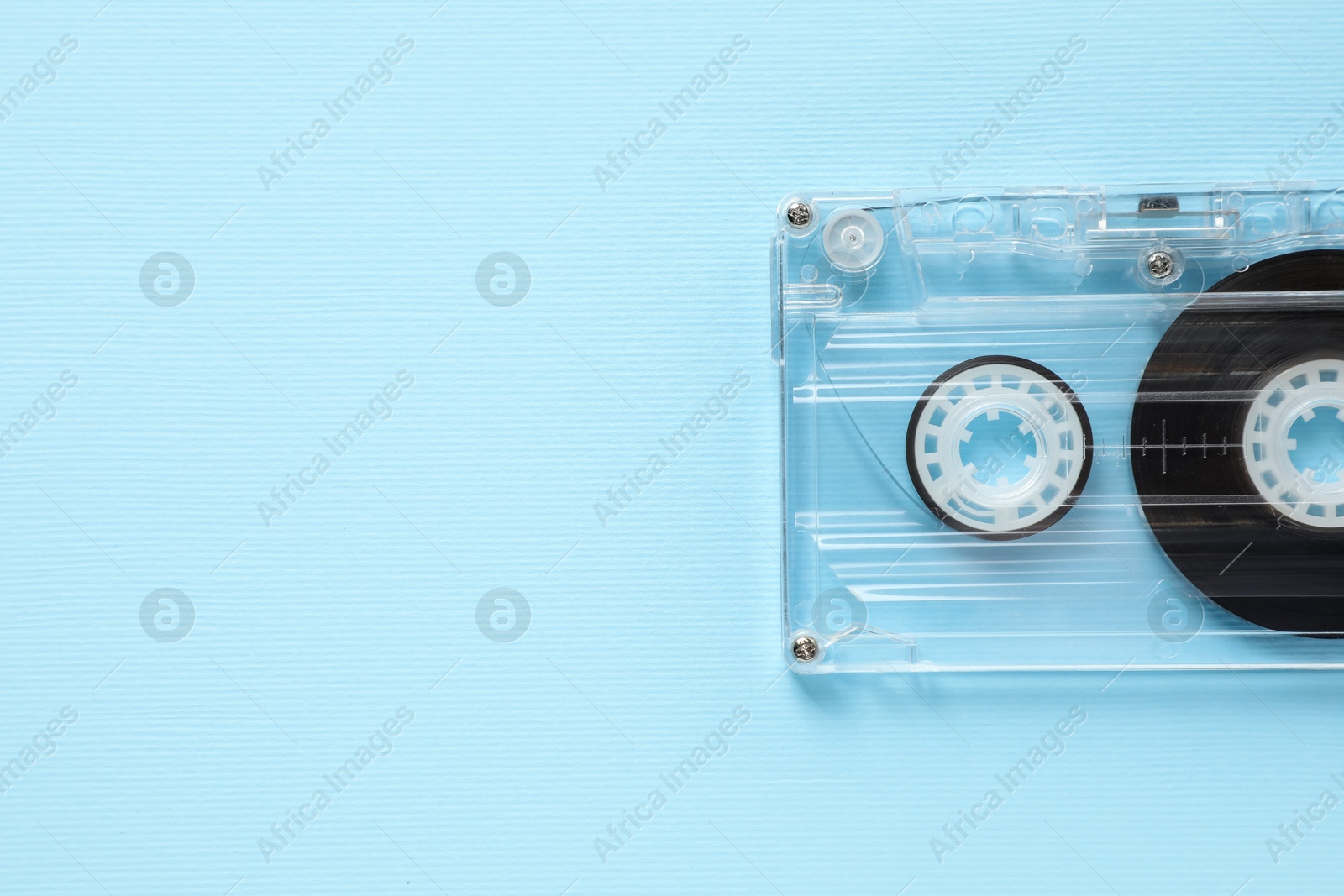 Photo of One audio cassette with magnetic tape on light blue background, top view. Space for text
