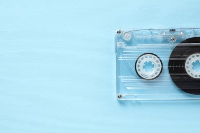 Photo of One audio cassette with magnetic tape on light blue background, top view. Space for text