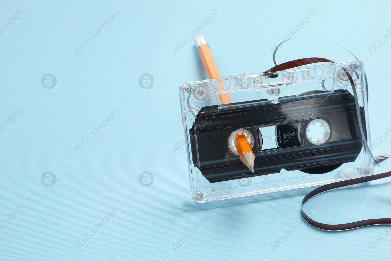 Photo of Rewinding audio cassette with pencil on light blue background, closeup. Space for text