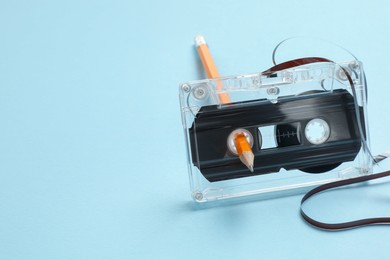 Photo of Rewinding audio cassette with pencil on light blue background, closeup. Space for text