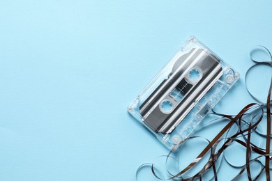 Photo of One audio cassette with magnetic tape on light blue background, top view. Space for text