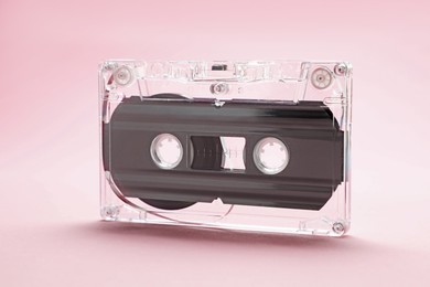 Photo of One audio cassette with magnetic tape on pink background, closeup