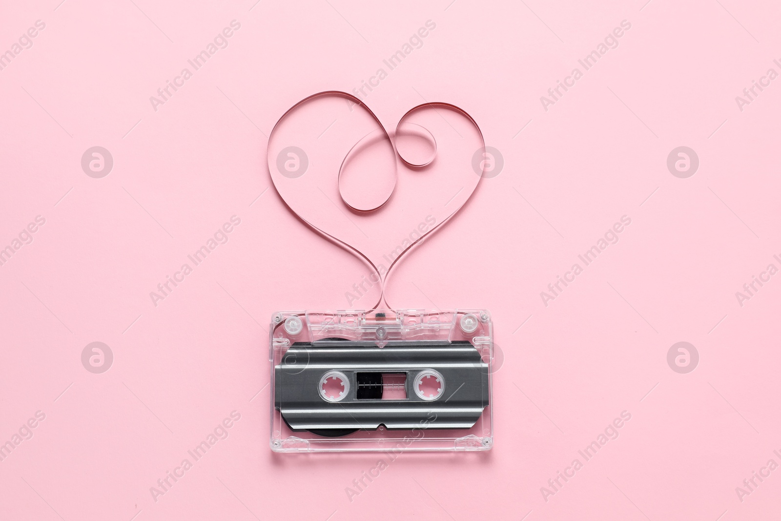 One audio cassette with heart shaped magnetic tape on pink background, top view Photo of One audio cassette with heart shaped magnetic tape on pink background, top view