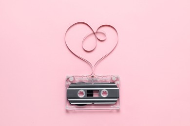 Photo of One audio cassette with heart shaped magnetic tape on pink background, top view