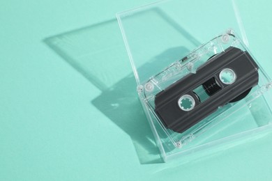 Photo of One audio cassette in open box on turquoise background, above view. Space for text