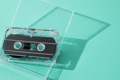 Photo of One audio cassette in open box on turquoise background, above view. Space for text