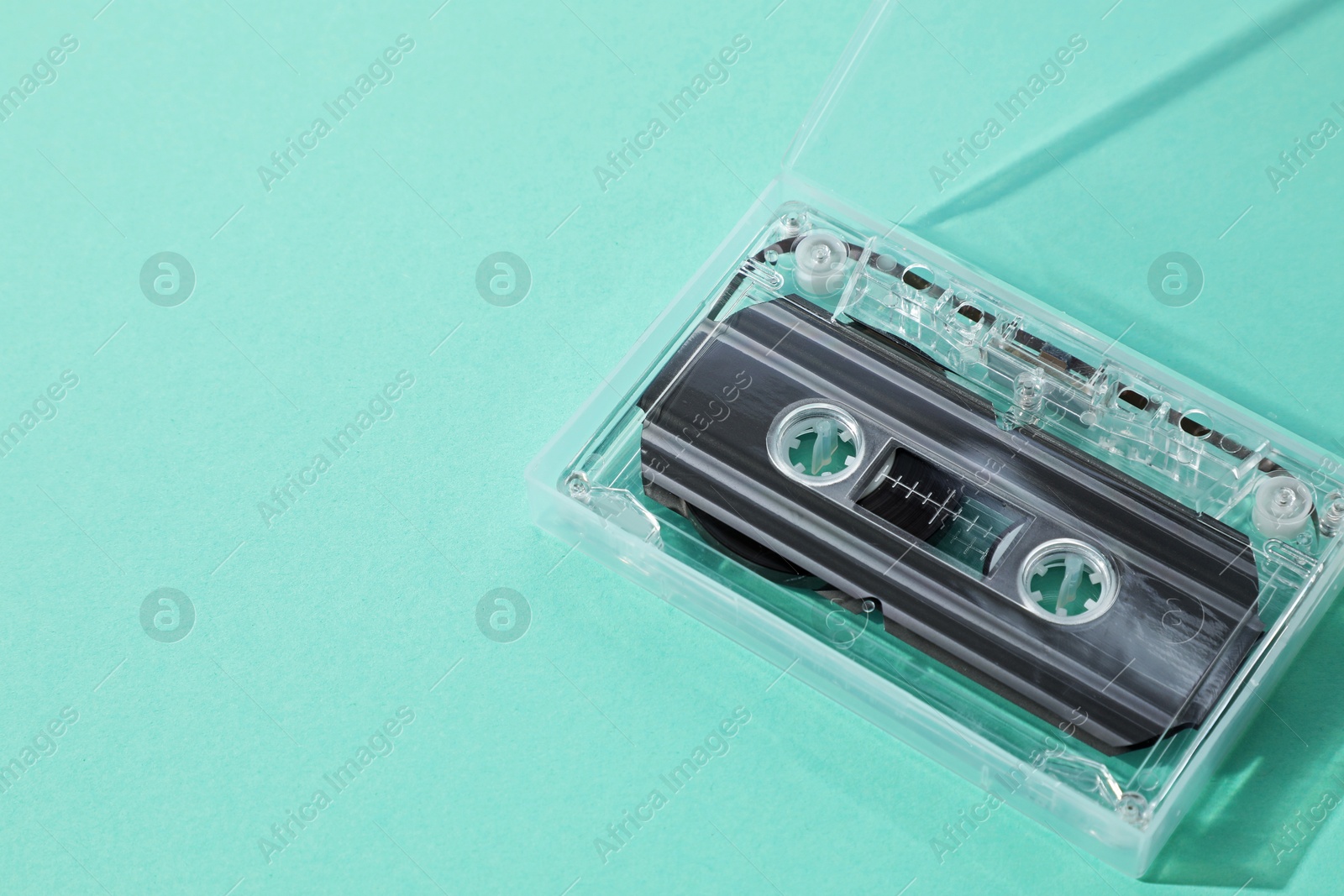 One audio cassette in open box on turquoise background, above view. Space for text Photo of One audio cassette in open box on turquoise background, above view. Space for text