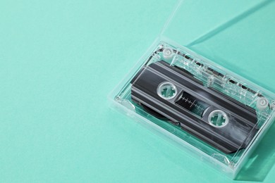 Photo of One audio cassette in open box on turquoise background, above view. Space for text