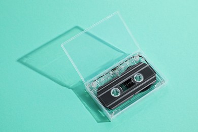 Photo of One audio cassette in open box on turquoise background, above view