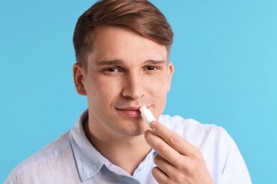 Photo of Young man applying lip balm onto his lips on light blue background