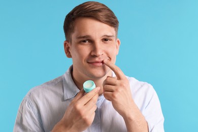 Photo of Young man applying lip balm onto his lips on light blue background