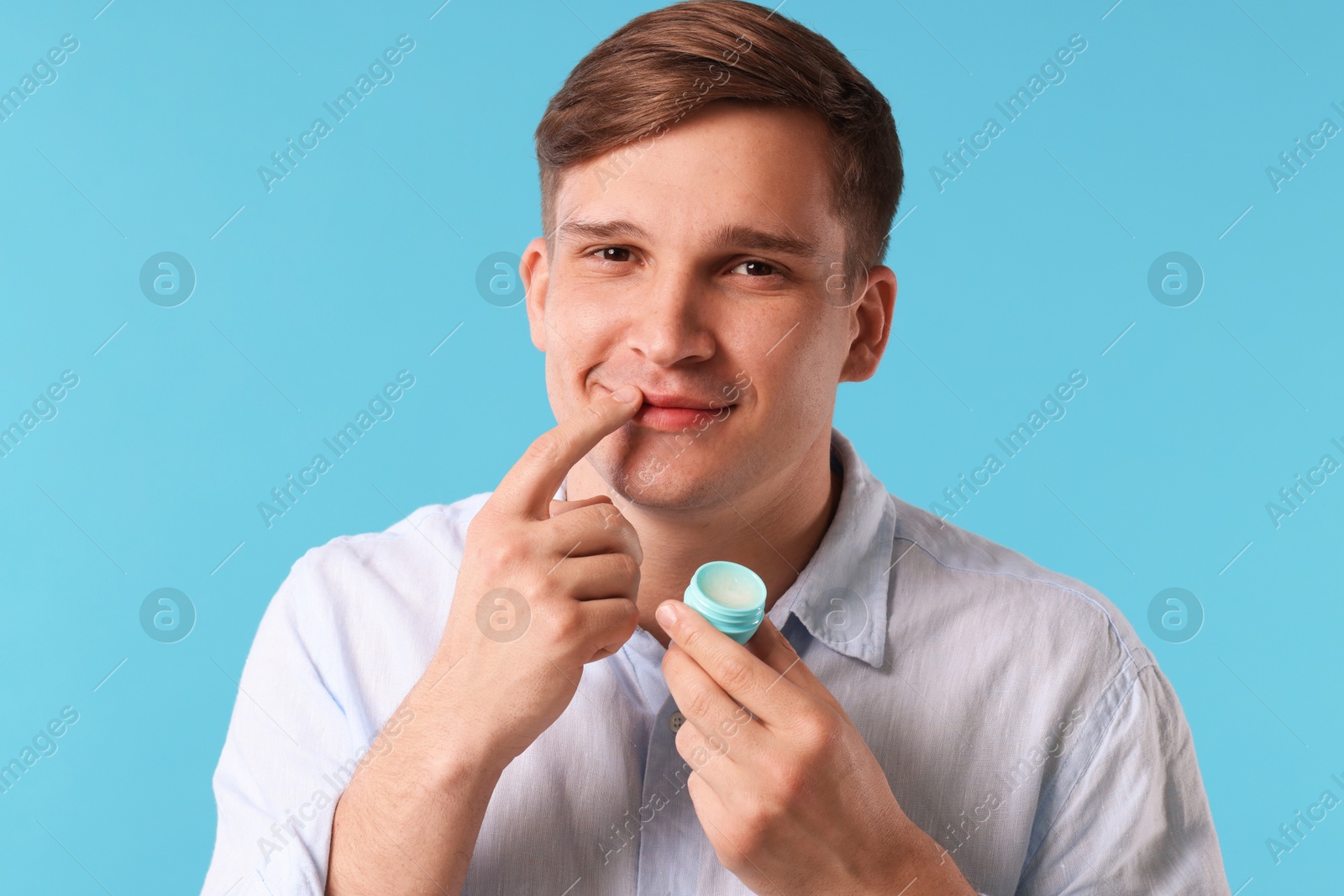 Young man applying lip balm onto his lips on light blue background Photo of Young man applying lip balm onto his lips on light blue background
