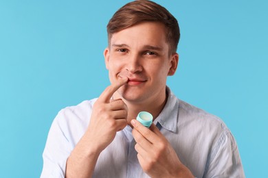 Photo of Young man applying lip balm onto his lips on light blue background