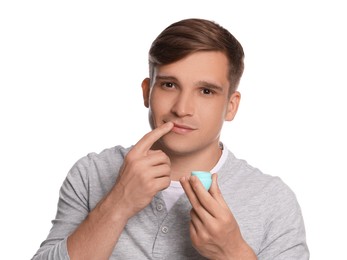 Photo of Young man applying lip balm onto his lips on white background