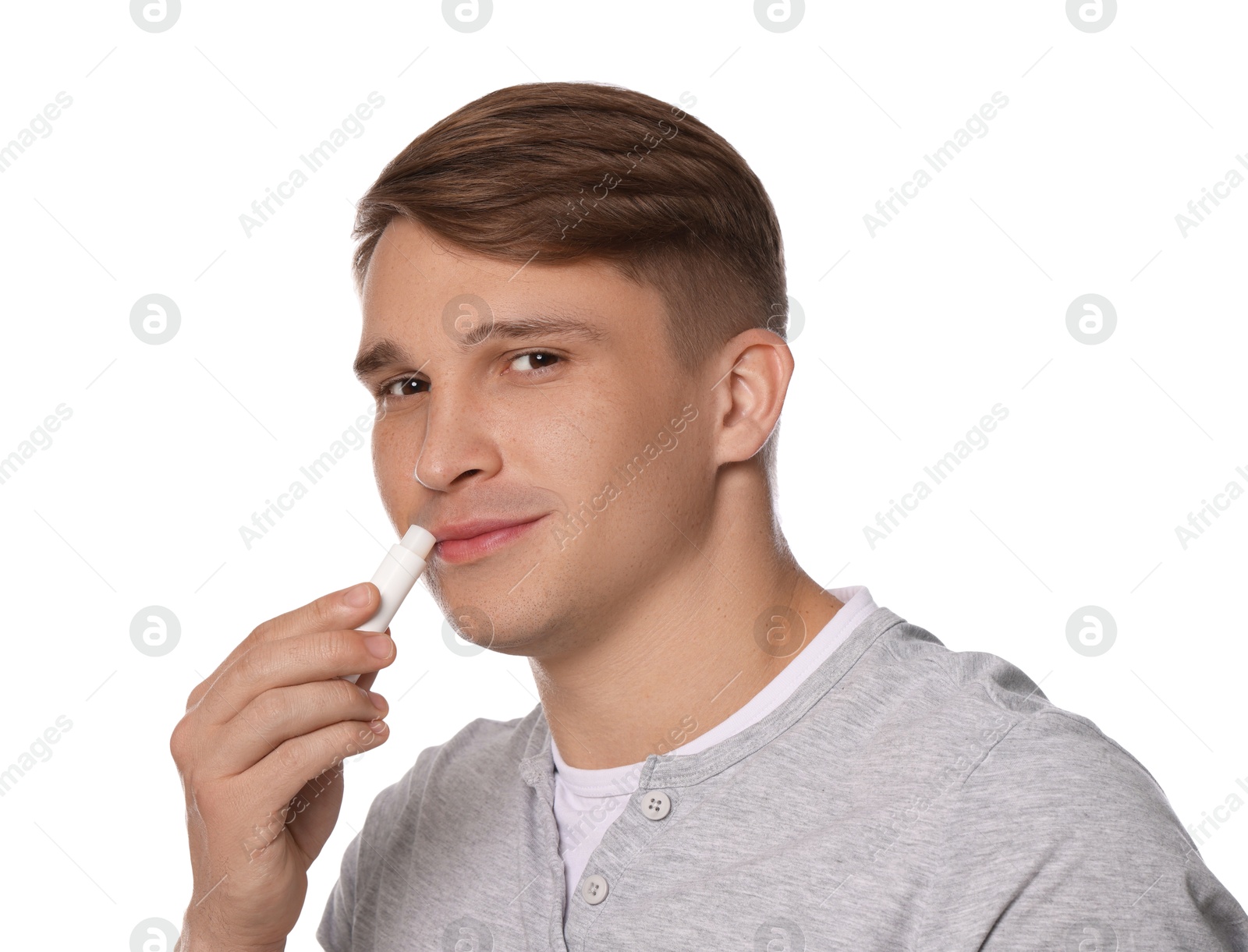 Young man applying lip balm onto his lips on white background Photo of Young man applying lip balm onto his lips on white background