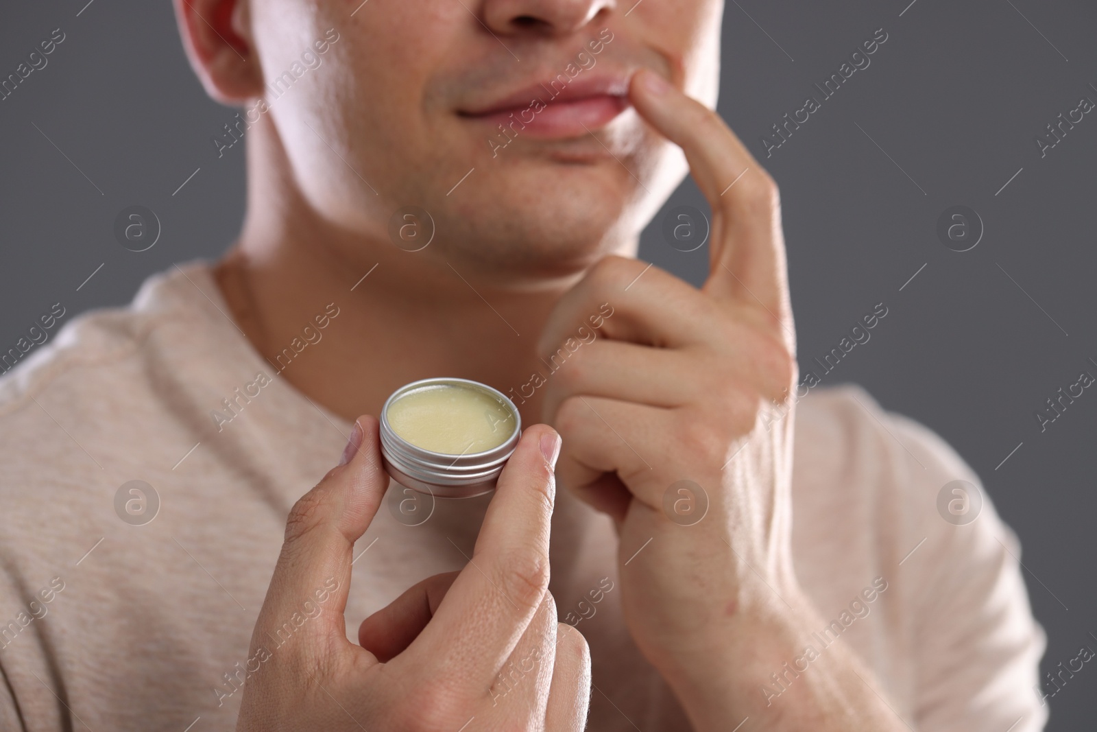 Young man applying lip balm onto his lips on grey background, closeup Photo of Young man applying lip balm onto his lips on grey background, closeup