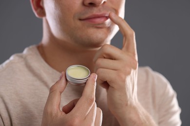 Photo of Young man applying lip balm onto his lips on grey background, closeup