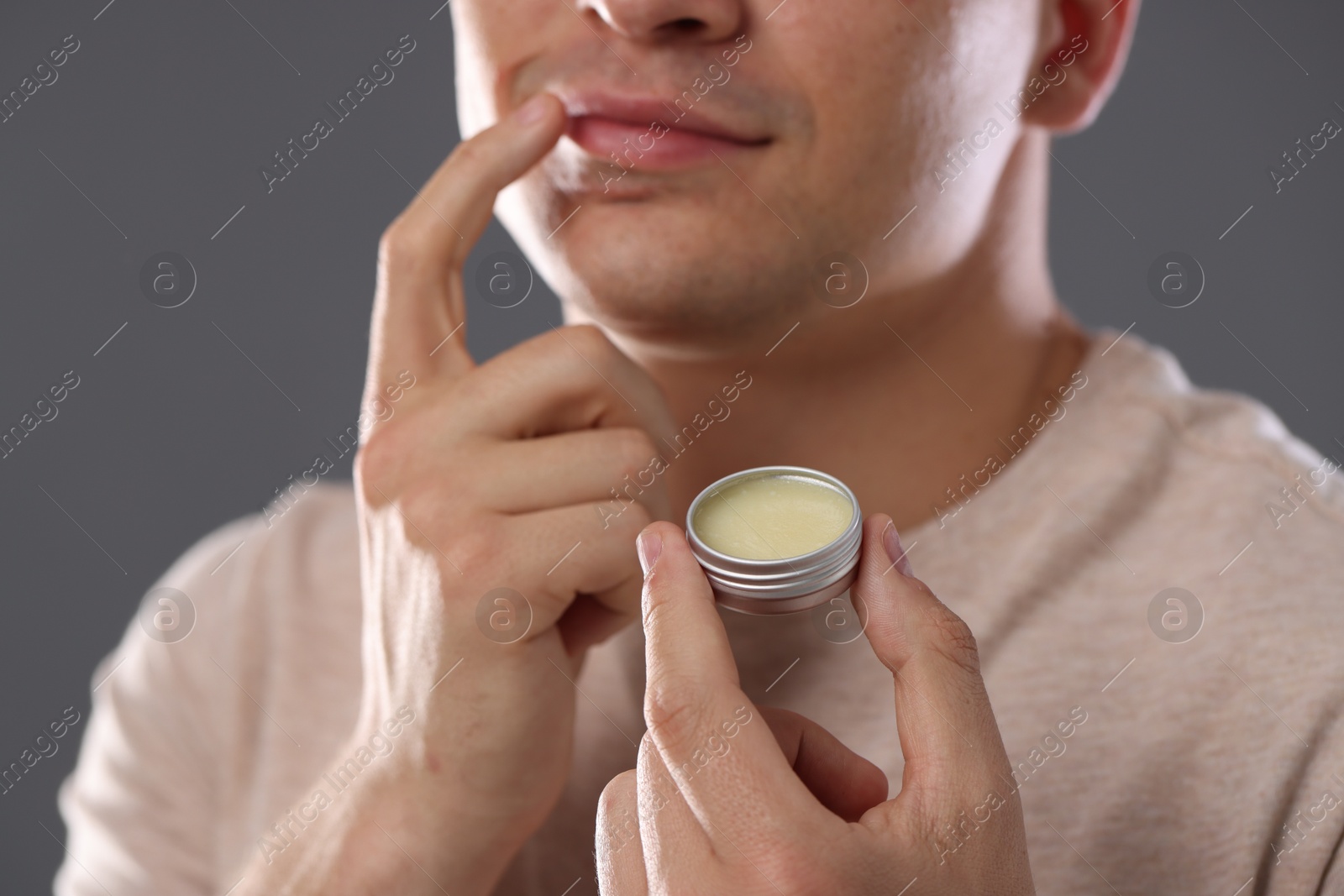 Young man applying lip balm onto his lips on grey background, closeup Photo of Young man applying lip balm onto his lips on grey background, closeup