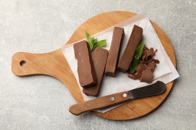 Photo of Pieces of tasty chocolate butter, shavings, mint and knife on grey textured table, top view