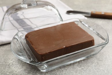 Photo of Block of tasty chocolate butter in glass keeper on grey textured table, closeup
