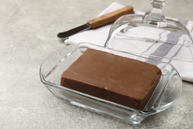 Photo of Block of tasty chocolate butter in glass keeper on grey textured table, closeup