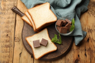 Photo of Tasty chocolate butter cubes, slices of bread and mint on wooden table, top view