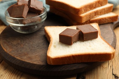 Photo of Tasty chocolate butter cubes on slice of bread on wooden table, closeup