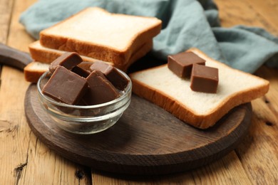 Photo of Tasty chocolate butter cubes and slices of bread on wooden table, closeup