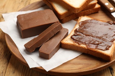 Photo of Pieces of tasty chocolate butter and slices of bread on wooden table, closeup