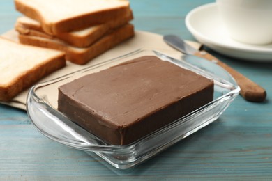 Photo of Block of tasty chocolate butter in glass keeper on light blue wooden table, closeup