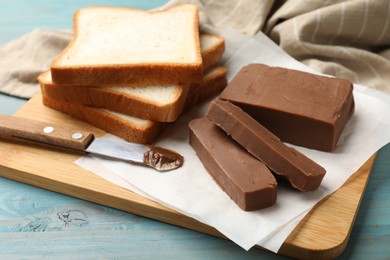 Photo of Pieces of tasty chocolate butter, slices of bread and knife on light blue wooden table, closeup