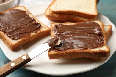 Photo of Pieces of bread with tasty chocolate butter and knife on light blue wooden table, closeup