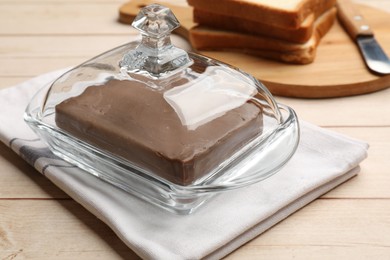 Photo of Block of tasty chocolate butter in glass keeper on light wooden table, closeup