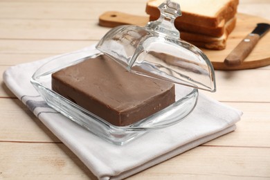 Photo of Block of tasty chocolate butter in glass keeper on light wooden table, closeup