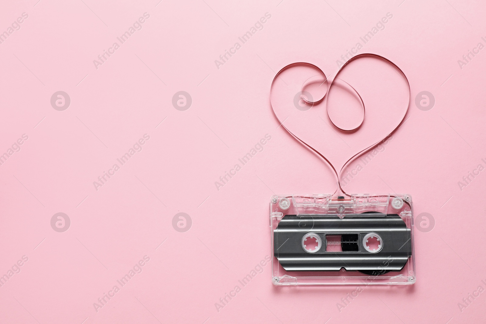 One audio cassette with heart shaped magnetic tape on pink background, top view. Space for text Photo of One audio cassette with heart shaped magnetic tape on pink background, top view. Space for text
