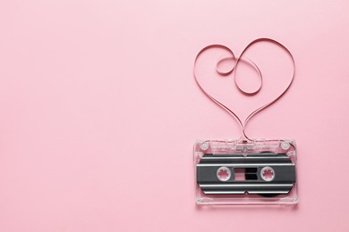 Photo of One audio cassette with heart shaped magnetic tape on pink background, top view. Space for text