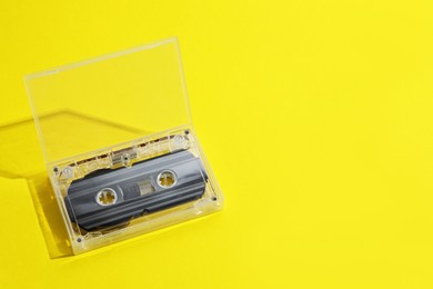 Photo of One audio cassette in open box on yellow background, above view. Space for text