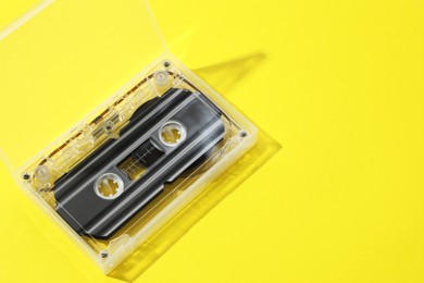 Photo of One audio cassette in open box on yellow background, above view. Space for text