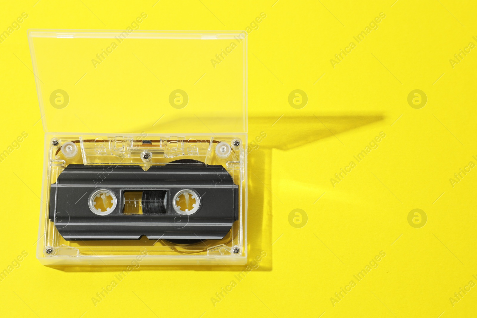 One audio cassette in open box on yellow background, above view. Space for text Photo of One audio cassette in open box on yellow background, above view. Space for text